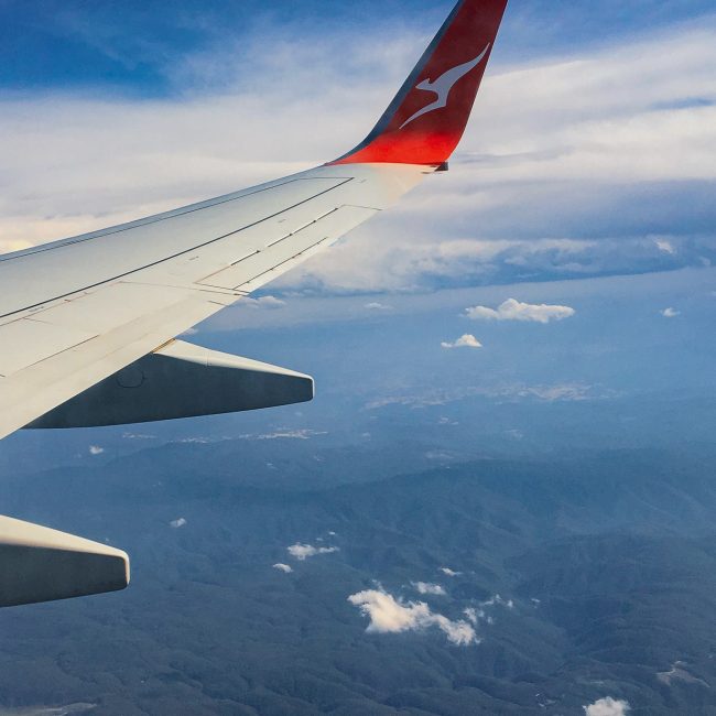 Image shows the view of liftoff from an airlplane window seat. Clouds are visible above craggy green mountains.