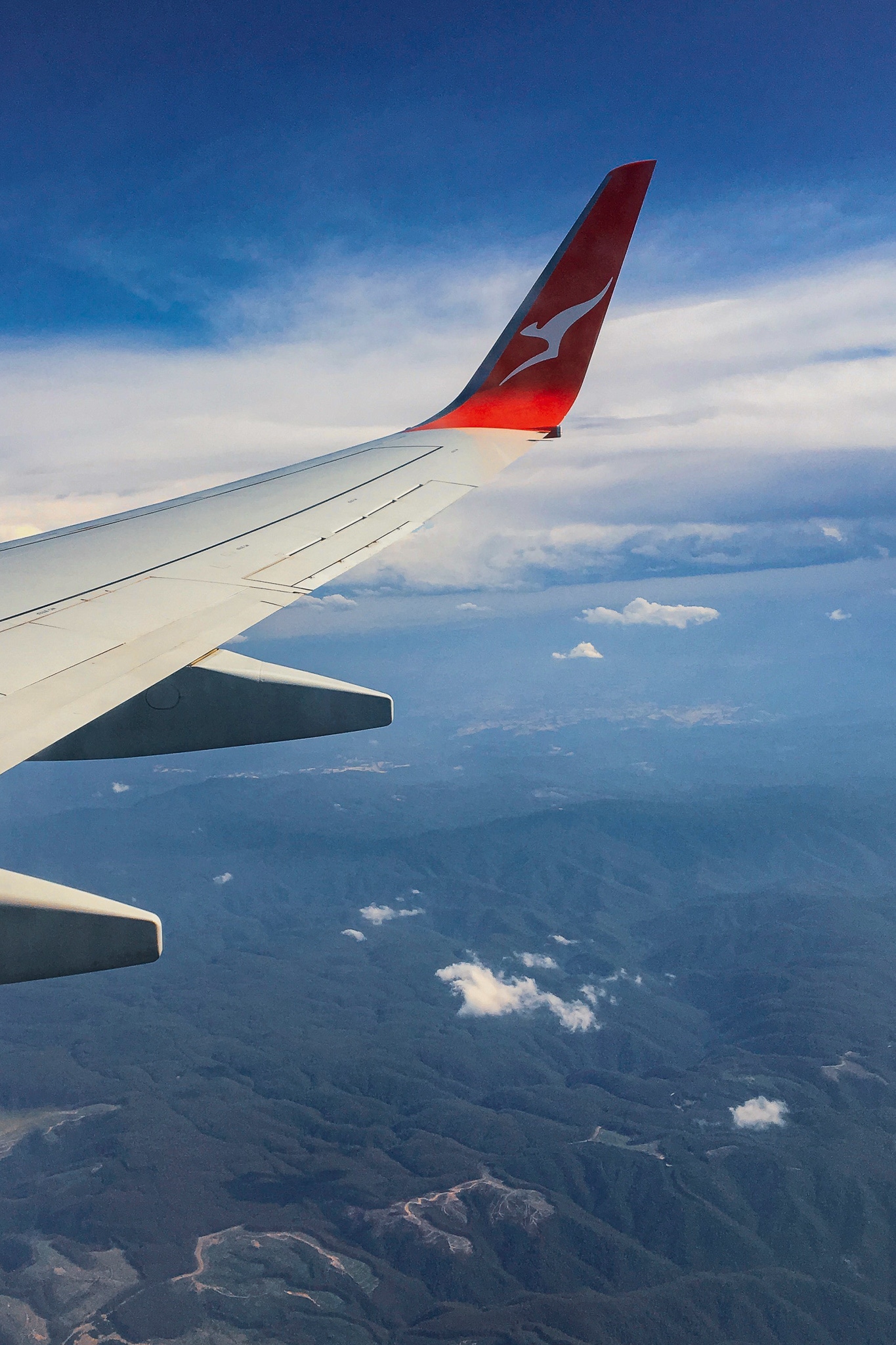 Image shows the view of liftoff from an airlplane window seat. Clouds are visible above craggy green mountains.